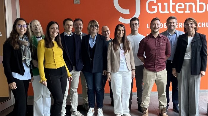lvh zu Gast in der Landesberufsschule Gutenberg in Bozen Gruppe von elf Personen steht vor orangefarbener Wand mit Gutenberg Logo