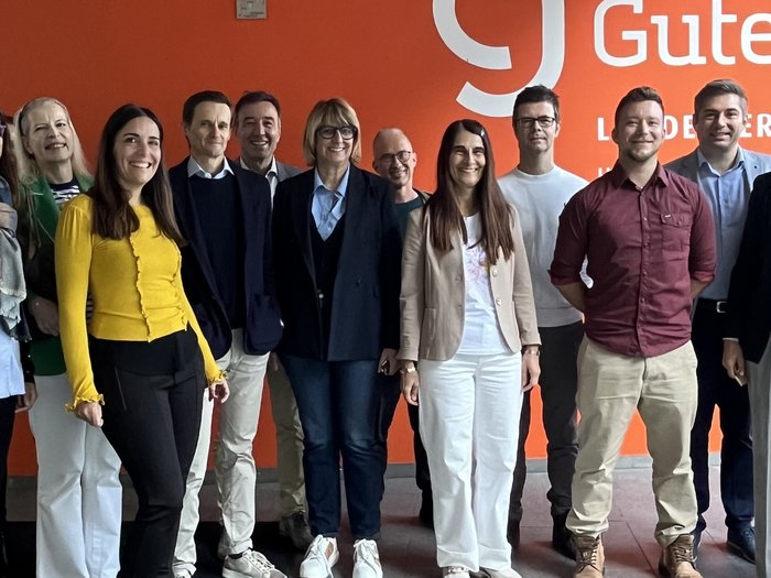 lvh zu Gast in der Landesberufsschule Gutenberg in Bozen Gruppe von elf Personen steht vor orangefarbener Wand mit Gutenberg Logo