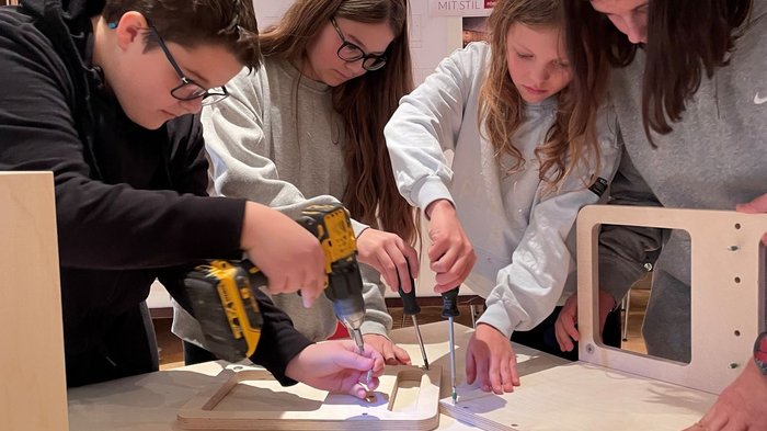 Mittelschüler mittendrin, in der Welt der praktischen Berufe Jugendliche bauen zusammen mit Werkzeug ein Möbelstück aus Holz zusammen