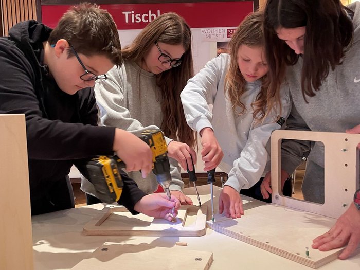 Mittelschüler mittendrin, in der Welt der praktischen Berufe Jugendliche bauen zusammen mit Werkzeug ein Möbelstück aus Holz zusammen