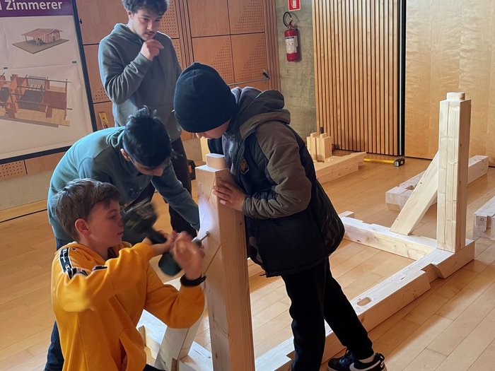 Mittelschüler mittendrin, in der Welt der praktischen Berufe Jugendliche bauen drinnen eine Holzkonstruktion zusammen