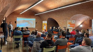 News Publikum hört einem Vortrag in einem Raum mit gewölbter Backstein-Decke zu