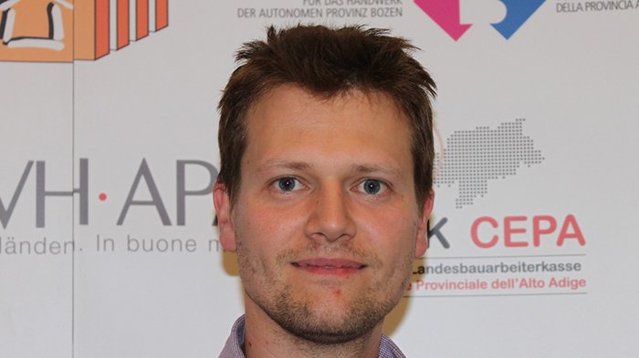 PKW-Hauptuntersuchungen und Führerscheine automatisch verlängert Porträt eines Mannes vor Werbebannern in Deutsch und Italienisch