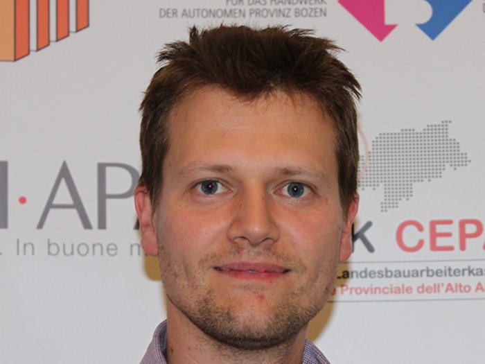 PKW-Hauptuntersuchungen und Führerscheine automatisch verlängert Porträt eines Mannes vor Werbebannern in Deutsch und Italienisch