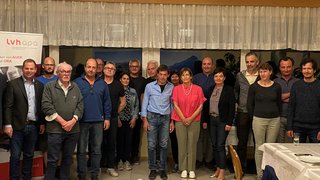 News Gruppenfoto von 21 Personen in einem Raum mit Tischen und Banner im Hintergrund