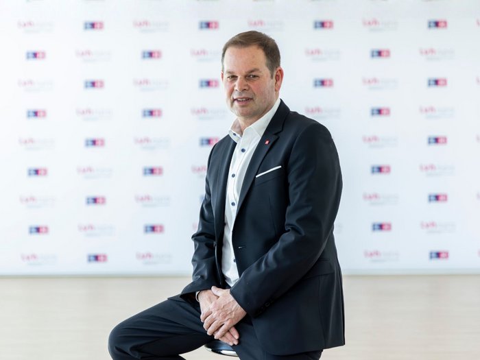 lvh begrüßt 500-Millionen-Investitionsprogramm für Bozen Mann im dunklen Anzug sitzt vor einer Wand mit wiederkehrenden Logos