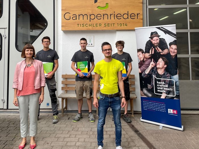 Lehrlingsmappe für Südtirols Tischlerbetriebe Gruppe von fünf Personen vor Gampenrieder Tischlerei mit Banner