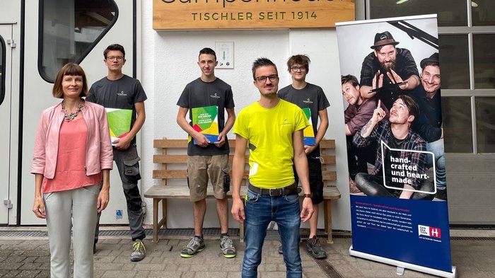 Lehrlingsmappe für Südtirols Tischlerbetriebe Gruppe von fünf Personen vor Gampenrieder Tischlerei mit Banner