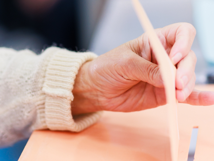 Gemeindewahlen 2025 Hand steckt Stimmzettel in Wahlurne bei einer Abstimmung