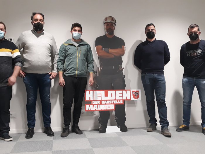 WorldSkills: il candidato dei muratori si presenta Cinque uomini con maschere accanto a sagoma di operaio edile con cartello Eroi del cantiere muratore