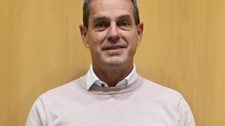 News Mittelalter Mann mit kurzem grauem Haar und rosa Pullover vor Holzwand