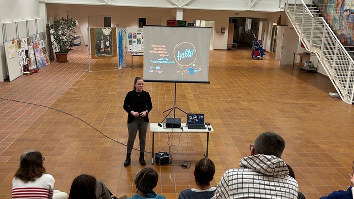 Einblicke in den Berufsalltag Frau hält Präsentation vor kleiner Gruppe in großem, hellem Raum mit Stufen