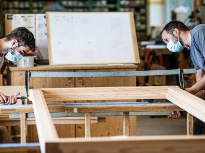 Kündigungsschutz hemmt Fachkräfteakquise Zwei Handwerker mit Masken arbeiten an einem Holzrahmen in einer Werkstatt.