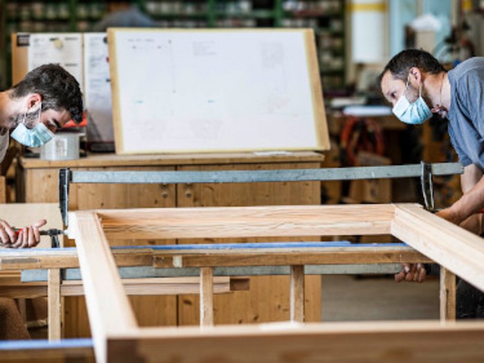 Kündigungsschutz hemmt Fachkräfteakquise Zwei Handwerker mit Masken arbeiten an einem Holzrahmen in einer Werkstatt.