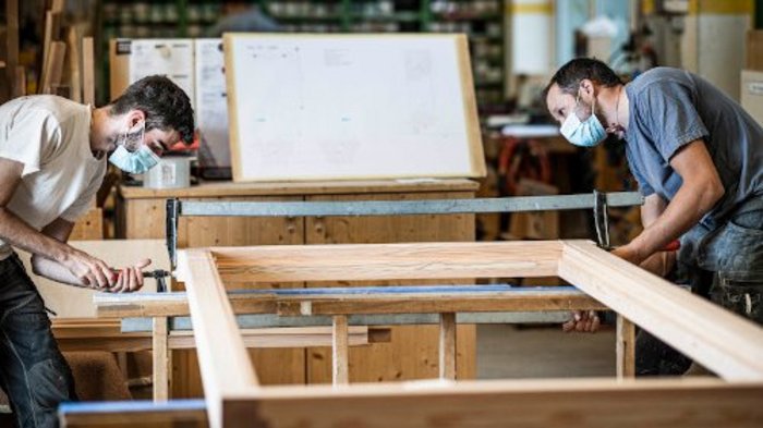 Kündigungsschutz hemmt Fachkräfteakquise Zwei Handwerker mit Masken arbeiten an einem Holzrahmen in einer Werkstatt.