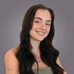 Das lvh-Team Junge Frau mit langen, dunklen Haaren und grünem Oberteil lächelt vor grauem Hintergrund