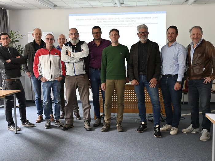 Eine konkrete Maßnahme zur Wettbewerbsfähigkeit des Sektors zur Unterstützung der Arbeitnehmer/innen und ihrer Familien Gruppe von elf Männern steht in einem Konferenzraum vor einer Präsentation