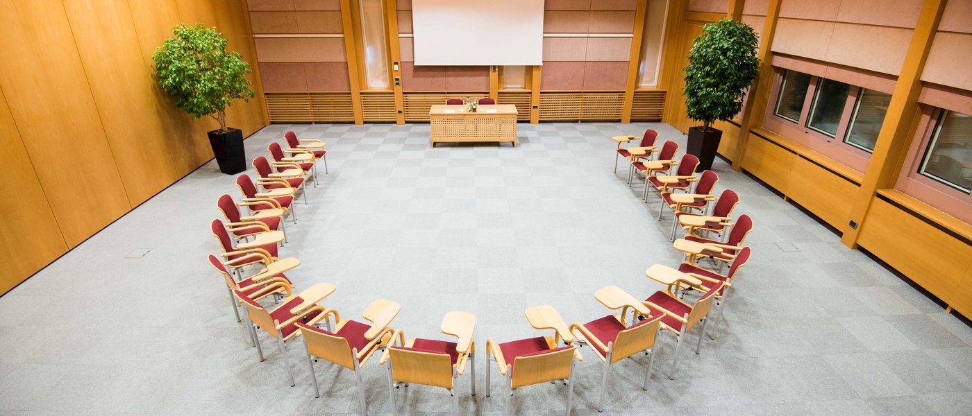 Vermietung Seminarräume Konferenzraum mit Stühlen im Halbkreis vor einem Tisch und einer Leinwand