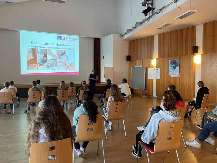 Berufe im Tourismus und Handwerk: spannend und kreativ! Gruppe Schüler sitzt mit Abstand in einem Saal vor einer Präsentation über Südtiroler Handwerk
