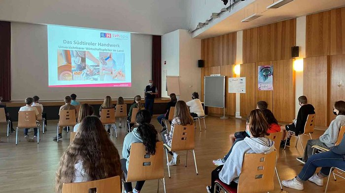 Berufe im Tourismus und Handwerk: spannend und kreativ! Gruppe Schüler sitzt mit Abstand in einem Saal vor einer Präsentation über Südtiroler Handwerk