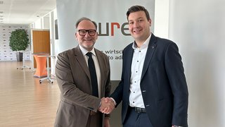 News Zwei Männer im Anzug geben sich in einem Büro die Hand