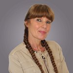 Das lvh-Team Frau mit zwei geflochtenen Zöpfen trägt eine beige Jacke vor grauem Hintergrund