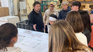 News Lehrer erklärt Schülern technische Zeichnungen in einer Werkstatt mit Holz und Maschinen