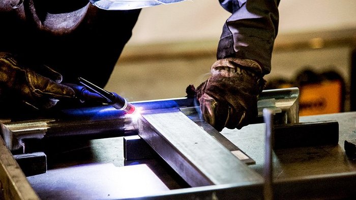 Volle Auftragsbücher, aber knappes und teures Material Person arbeitet mit Schutzkleidung und Schweißgerät an Metallrahmen