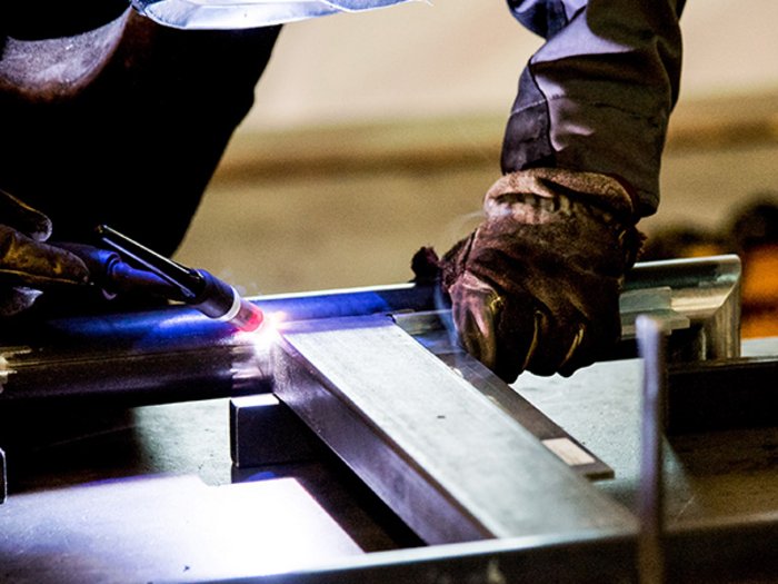 Volle Auftragsbücher, aber knappes und teures Material Person arbeitet mit Schutzkleidung und Schweißgerät an Metallrahmen