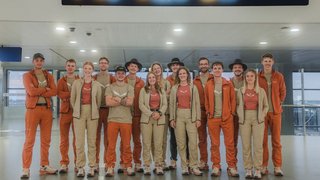 News Gruppo di 14 persone con abiti arancioni e beige in un ambiente interno