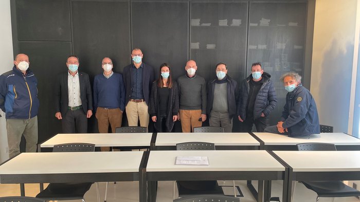 Bauarbeiterkasse: neue Vereinbarung für die Arbeitskleidung Gruppe von zehn Personen mit Masken in einem Besprechungsraum hinter Tischen
