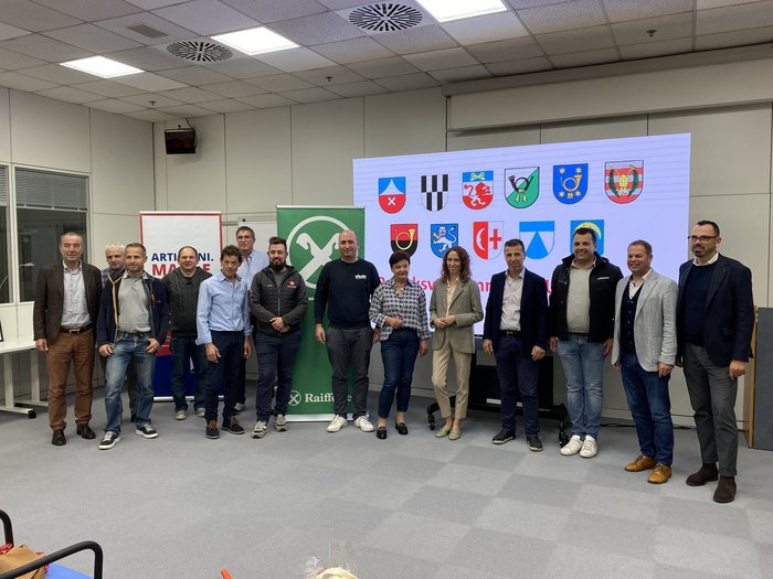 Riunione del circondario Bassa Atesina di lvh.apa: approfondimenti, prospettive e riconoscimenti Gruppo di persone in una stanza davanti a striscioni e uno schermo con stemmi