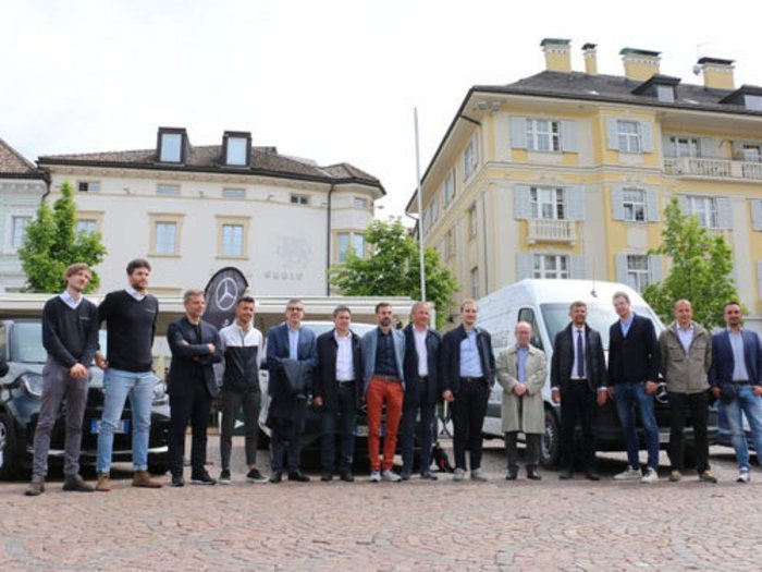 eTestDays – 67 Südtiroler Betriebe starten emissionsfrei in den Mai Gruppe von Männern in formeller Kleidung vor Gebäuden und Autos auf Kopfsteinpflaster