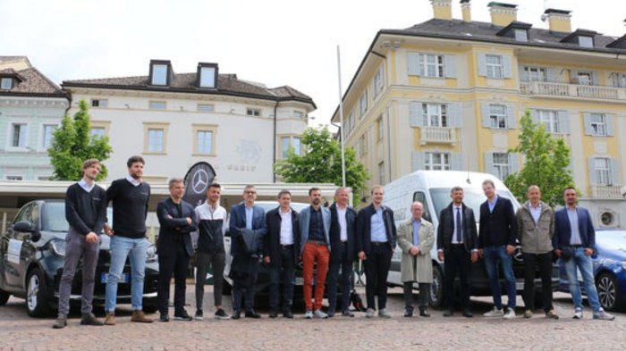 eTestDays – 67 Südtiroler Betriebe starten emissionsfrei in den Mai Gruppe von Männern in formeller Kleidung vor Gebäuden und Autos auf Kopfsteinpflaster