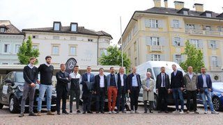 News Gruppe von Männern in formeller Kleidung vor Gebäuden und Autos auf Kopfsteinpflaster