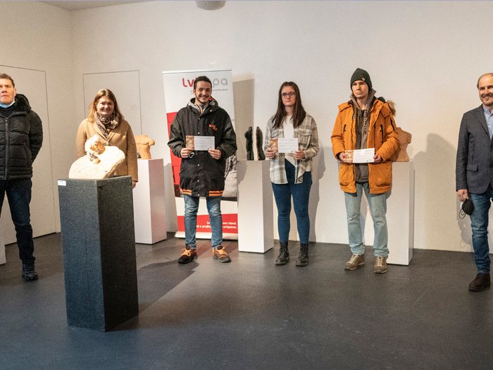„Kunst ist schön“ Gruppe von sechs Personen in einer Galerie mit Skulpturen, drei halten Zertifikate