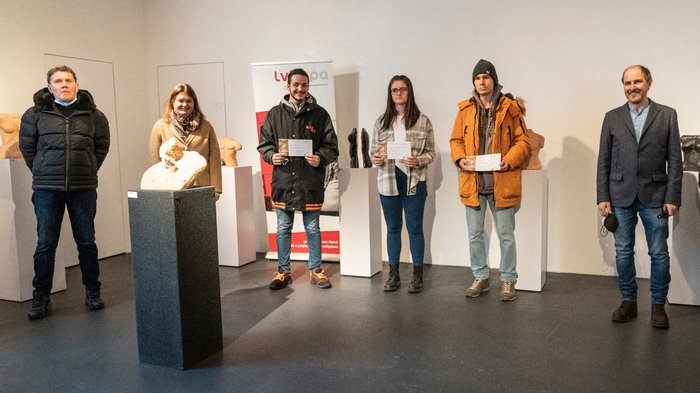 „Kunst ist schön“ Gruppe von sechs Personen in einer Galerie mit Skulpturen, drei halten Zertifikate