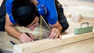 News Mann trägt Gehörschutz und zeichnet mit Geodreieck auf Holzstück