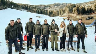 News Gruppe von zehn Personen in Winterjacken auf schneebedecktem Hang vor Wald und Bergen