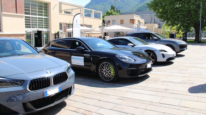 eTestDays - Südtirols Wirtschaft unter Strom Vier sportliche Autos vor einem modernen Gebäude bei sonnigem Bergwetter