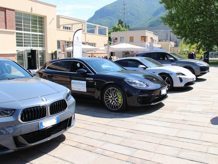 eTestDays - Südtirols Wirtschaft unter Strom Vier sportliche Autos vor einem modernen Gebäude bei sonnigem Bergwetter