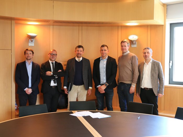 Bauaufträge: Lösung gefunden, damit Betriebe weiterarbeiten können Sechs Männer in Geschäftskleidung stehen in einem Besprechungsraum vor einem runden Tisch