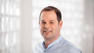 News Porträt eines Mannes mit blauem Hemd vor hellem unscharfem Hintergrund