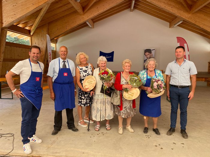 Ehrung der ältesten anwesenden Frauen © lvh.apa Gruppe von Menschen in einer Holzhütte mit Blumen und hölzernen Auszeichnungen