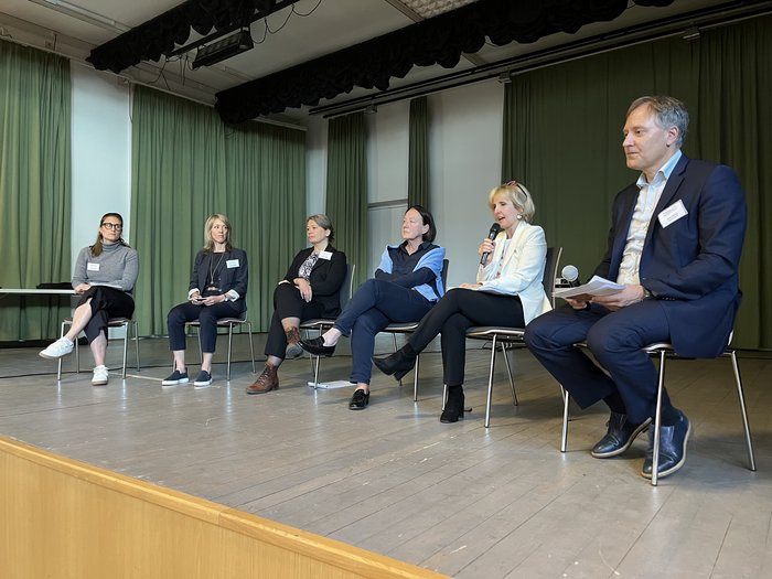 Wohnen muss leistbar und nachhaltig werden Sechs Personen auf einer Bühne in einem Podiumsgespräch mit Mikrofonen