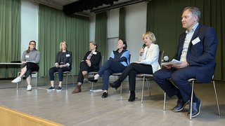 News Sechs Personen auf einer Bühne in einem Podiumsgespräch mit Mikrofonen