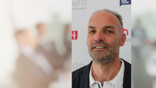 News Porträt eines lächelnden Mannes vor einem Werbeplakat mit Text