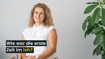 Jobs Frau in weißem Oberteil sitzend neben einer Pflanze vor weißer Wand