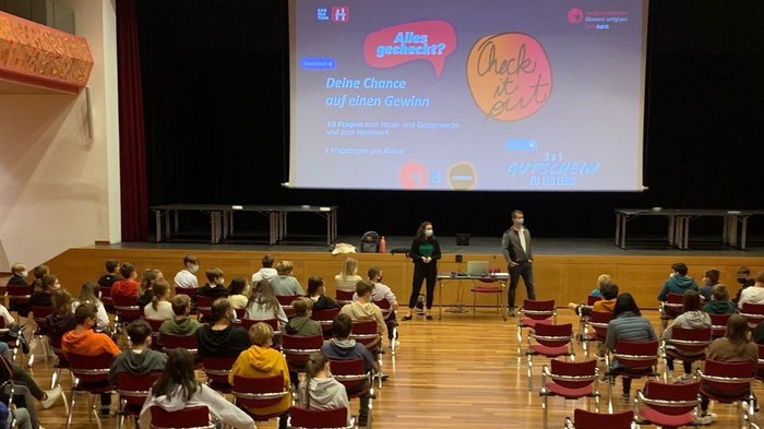 I mestieri nell’artigianato e nel turismo? Appassionanti e creativi! Studenti con mascherine seduti in una sala ascoltano una presentazione su uno schermo grande