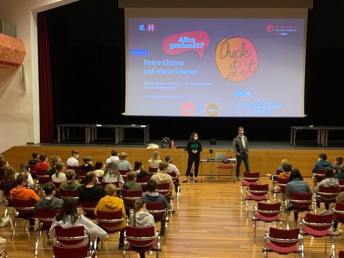 I mestieri nell’artigianato e nel turismo? Appassionanti e creativi! Studenti con mascherine seduti in una sala ascoltano una presentazione su uno schermo grande